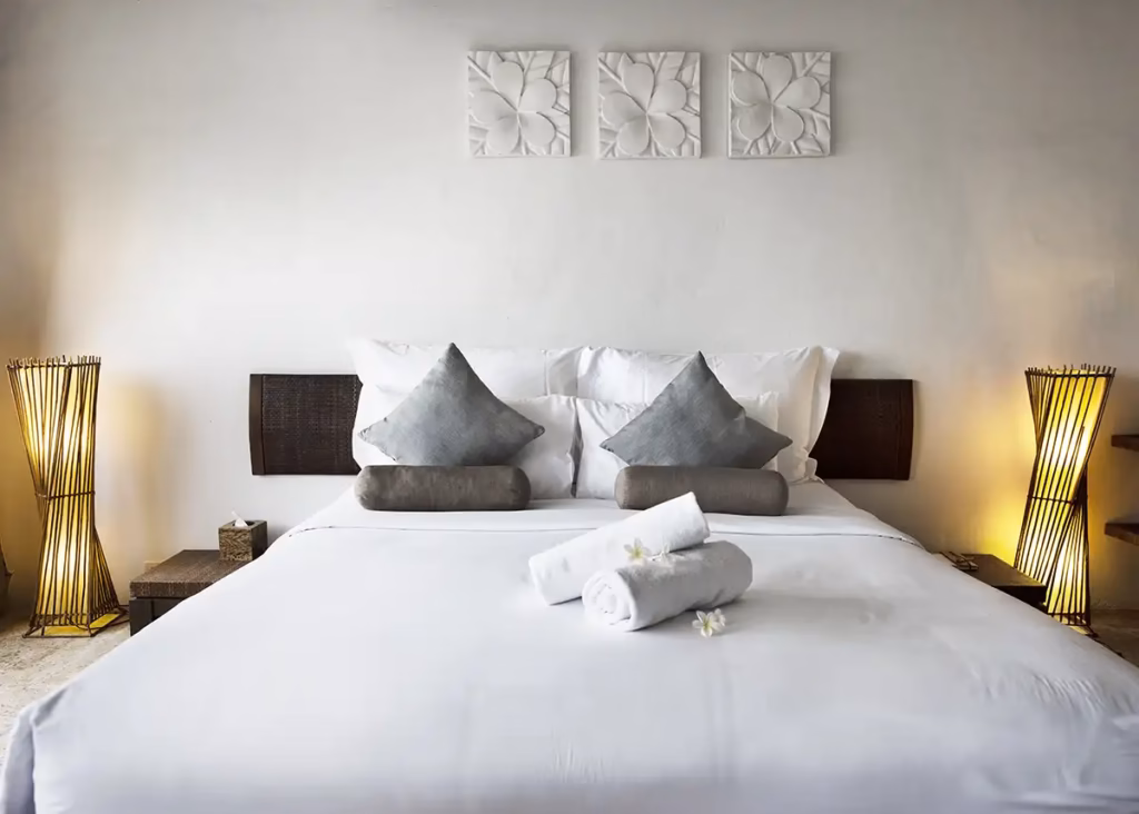 Quarto de hotel premium com cama branca impecavelmente feita, lençóis e almofadas alinhadas, tons claros e iluminação suave.