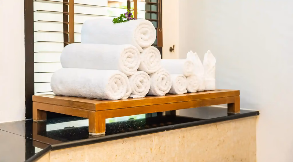 Descubra o modelo Hotelaria 360º: como alinhar roupa de cama, toalhas e fardas para otimizar operações, reduzir custos e melhorar as reviews do seu hotel. 4 Toalha turca branca sobre uma superfície de casa de banho, com textura suave e acabamento premium.